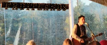 Mary Guathier with a guitar in front of the Fruitlands sign