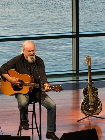 a man holding a guitar in front of a body of water